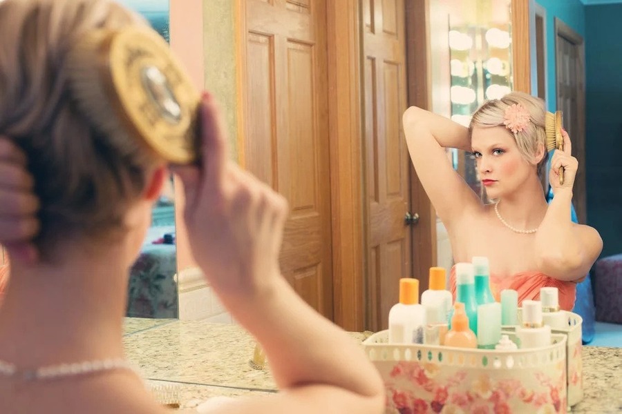 Woman using a hairbrush in front of a bathroom mirror