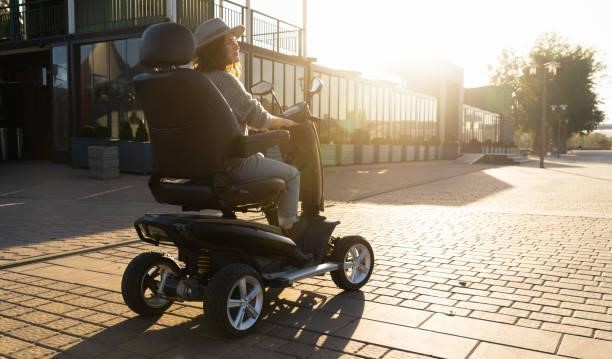 Woman tourist riding a four wheel mobility electric scooter Woman tourist riding a four wheel mobility electric scooter on a city street. riding a wheelcahir scooter stock pictures, royalty-free photos & images