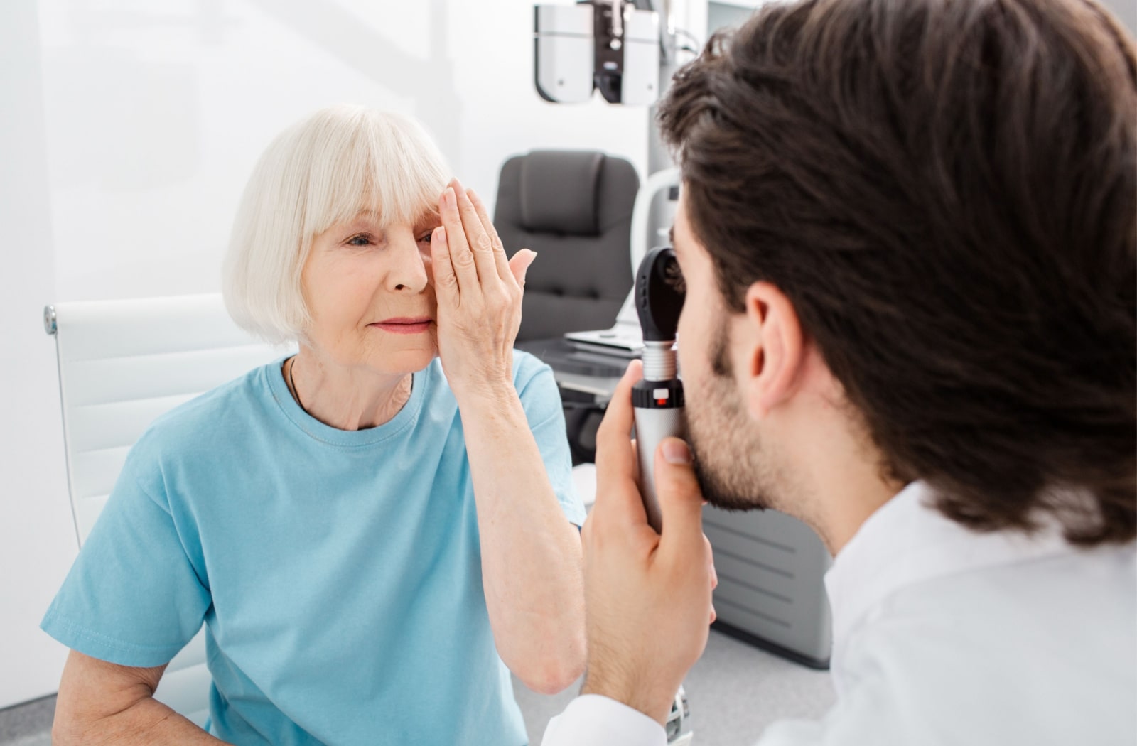 An older female patient covering her left eye with her left hand as the optometrist examines her other eye