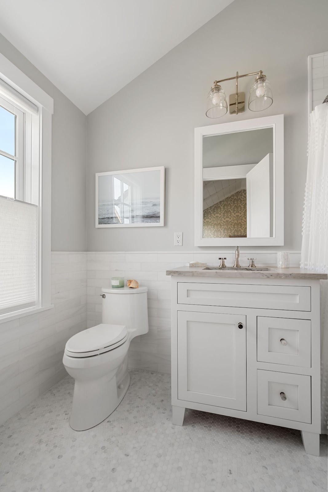 The picture depicts a bathroom with white tile flooring and gray walls. The sink includes white cabinets, a marble countertop, and a golden light fixture.