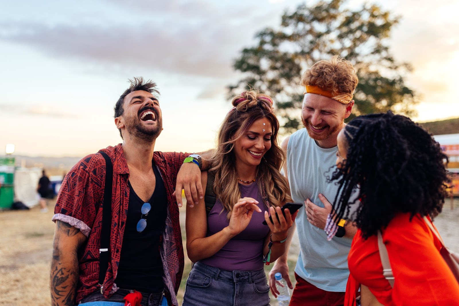 Um grupo de quatro jovens que riem e conversam entre si. Eles estão em um festival de música a céu aberto