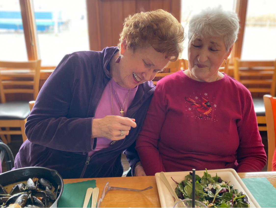 Two woman smiling with their eyes closed while eating food in front of them