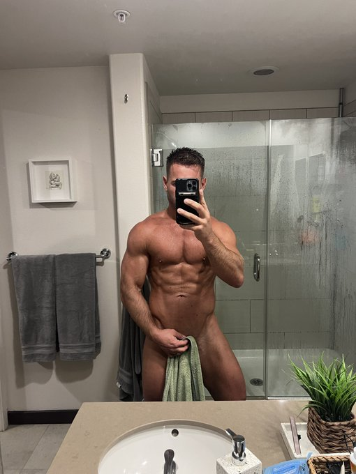 Sumner Blayne posing in front of the bathroom mirror for an iphone mirror selfie while posing with a towel over his flaccid cock