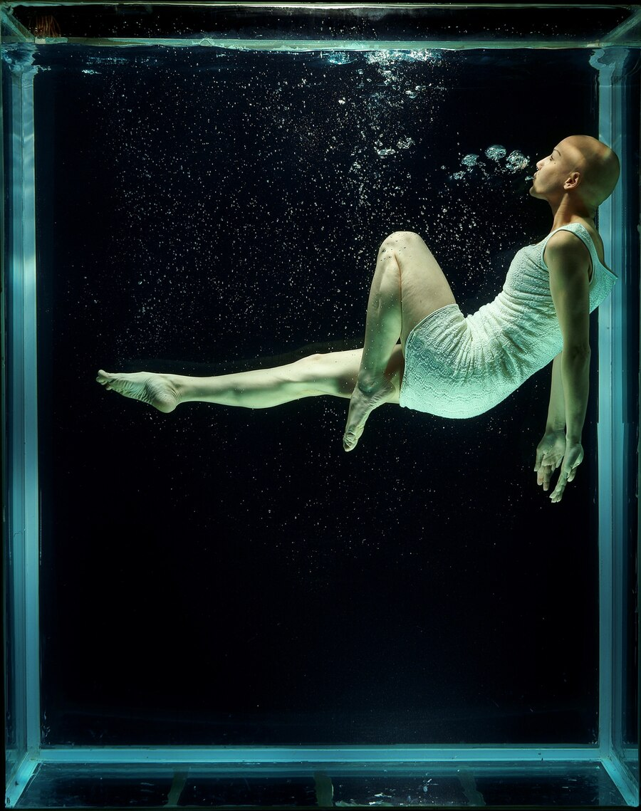 A person underwater in a glass box.
