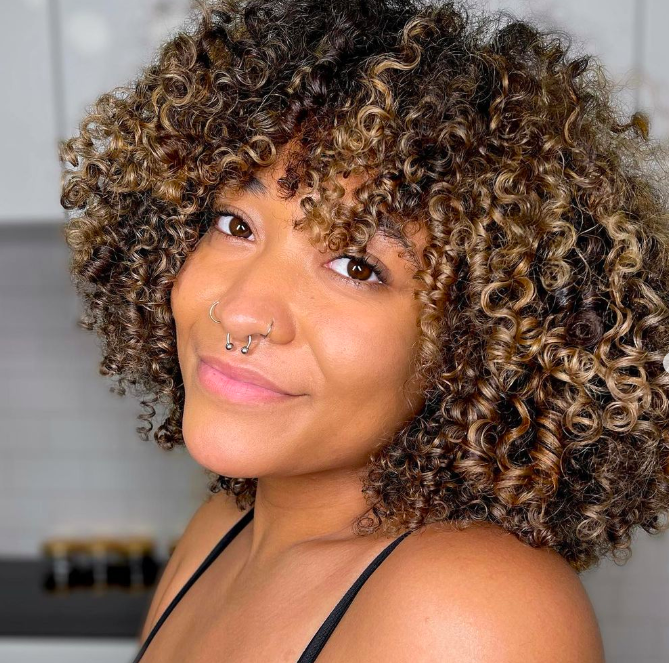 A person with curly hair and a nose ring

Description automatically generated