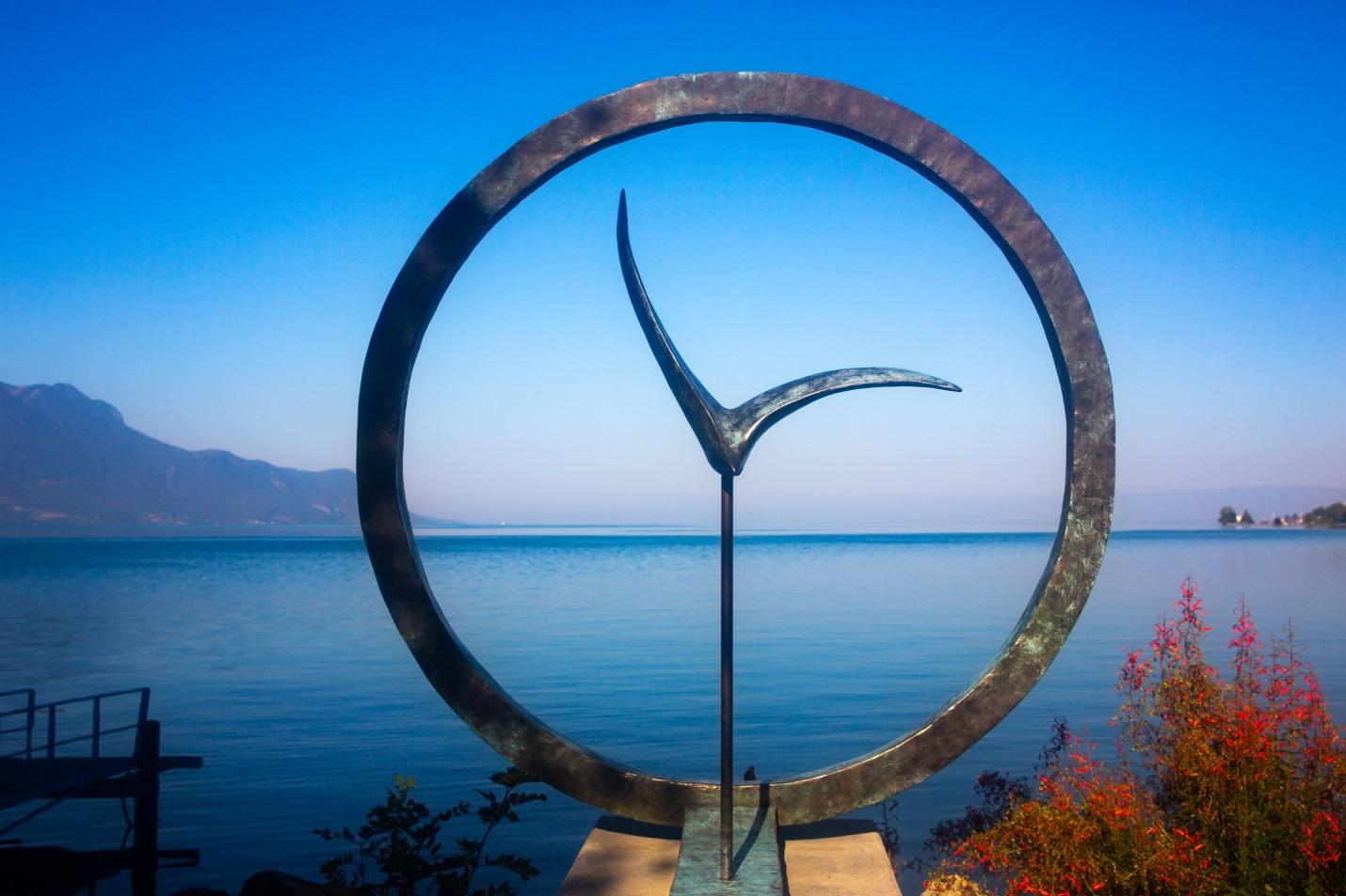 A sculpture of a bird in a circle by the water

Description automatically generated