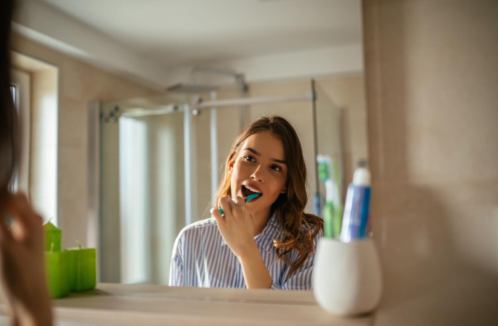 A woman in a striped shirt brushing her teeth in front of a mirror.
