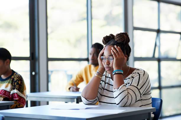 worried student sitting with head in hands at desk - black woman stress stock pictures, royalty-free photos & images