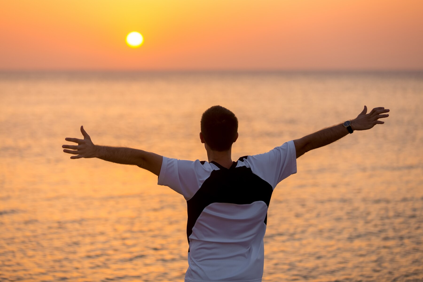 A man raising hands near sea at sunset thinking about life quotes.