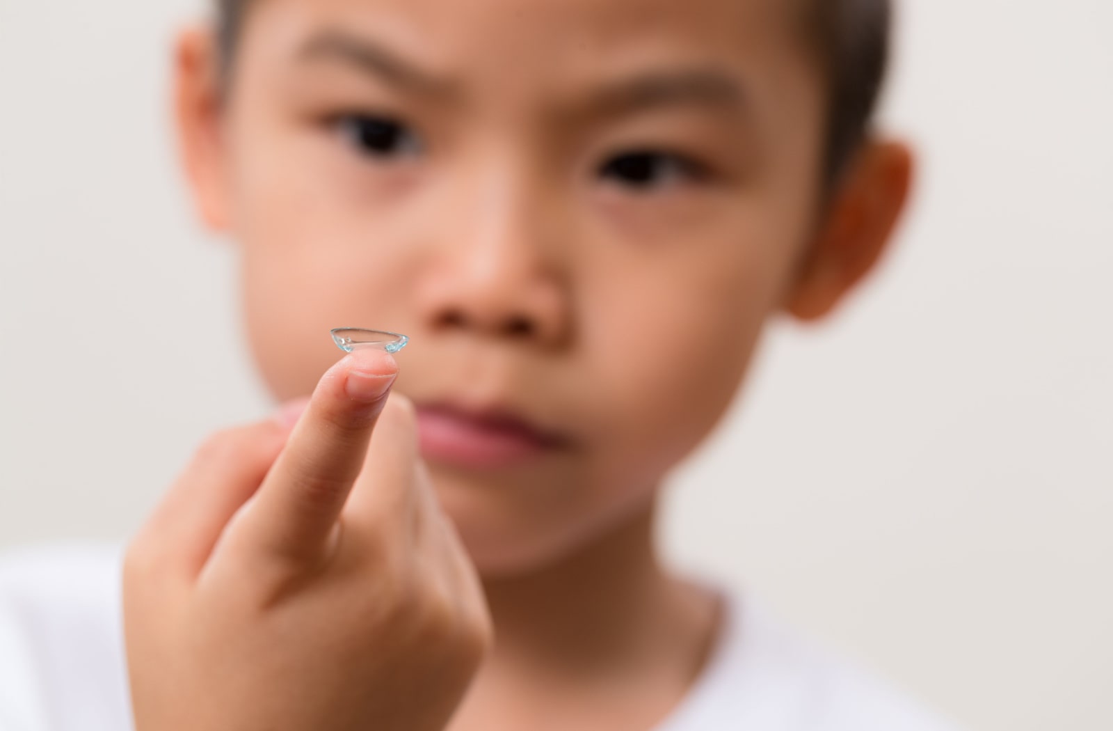 A young boy holds out a contact lens on his right index finger