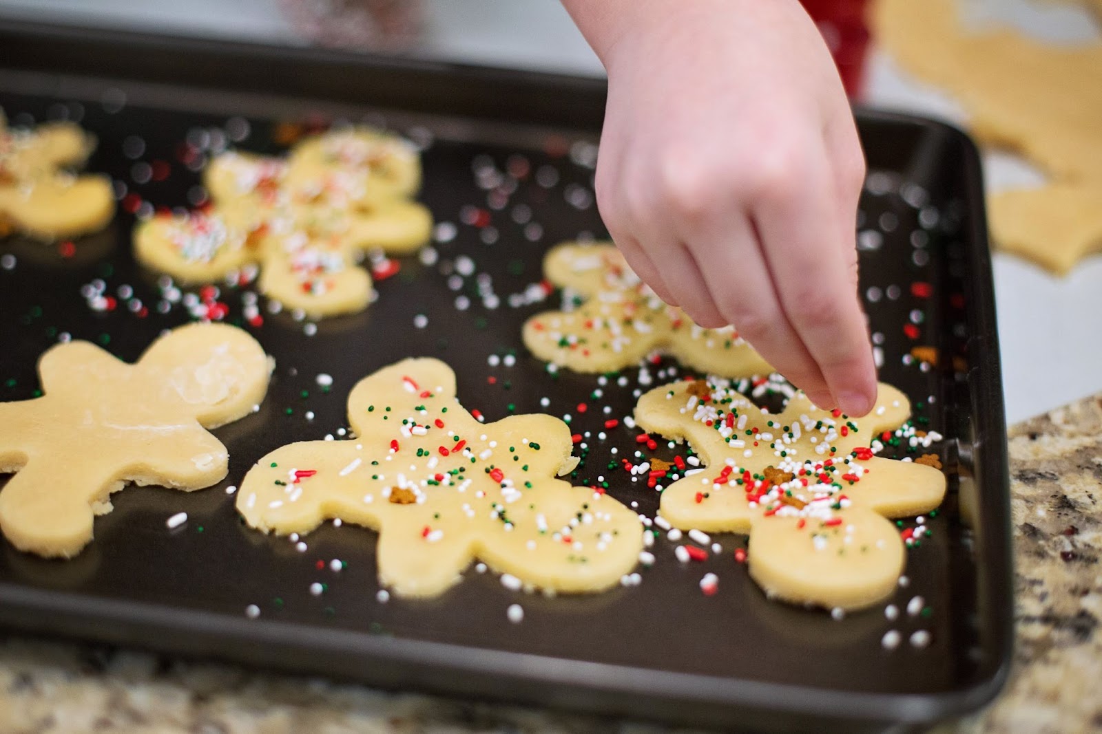 Freshly baked gingerbread sugar cookies on a baking sheet, adorned with festive red and white sprinkles for a delightful holiday treat.