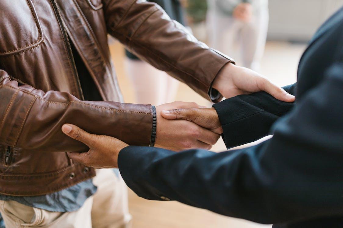 free person in black suit shaking hand with a person in brown leather jacket stock photo