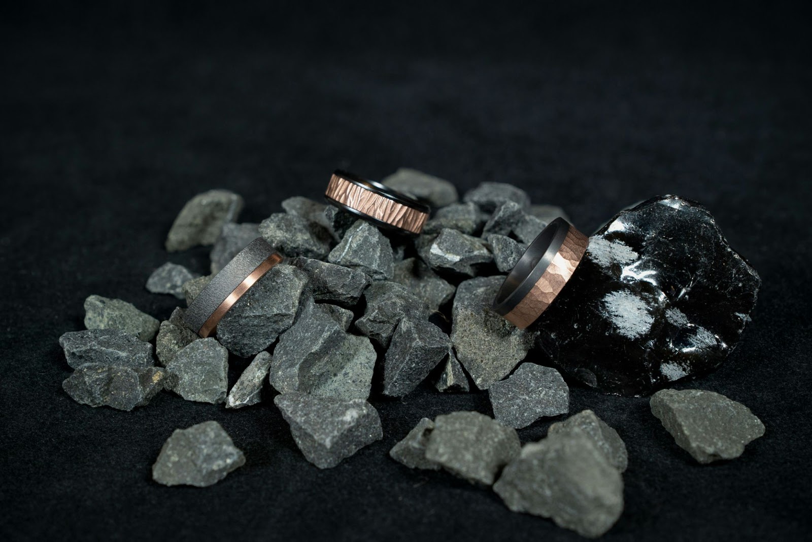 Three mixed materials mens weddings bands laying on rocks.