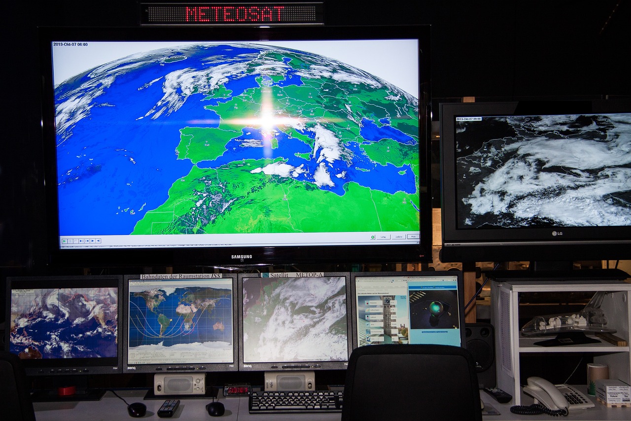 Control room with multiple monitors displaying global weather patterns and satellite imagery, utilized for real-time weather data for energy management.
