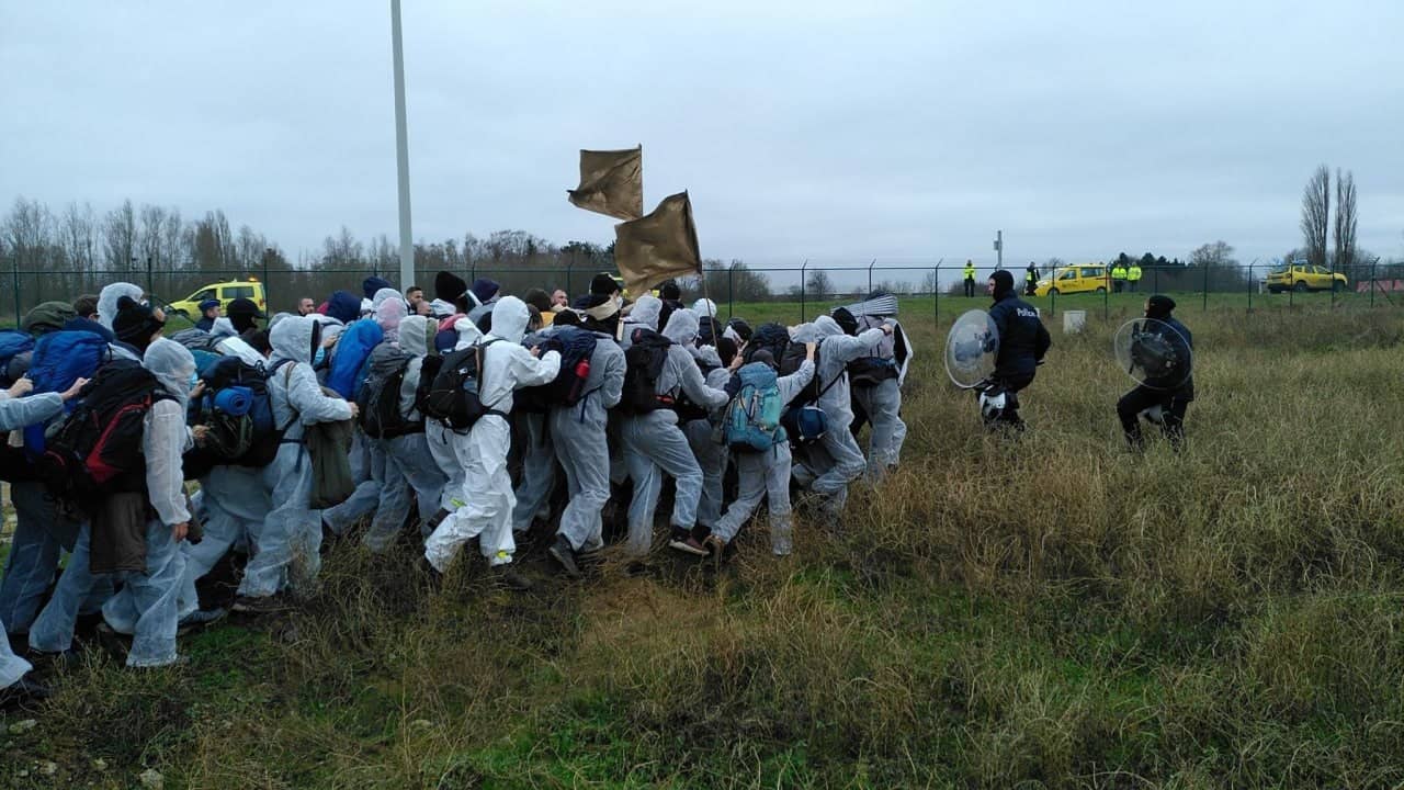 A "finger" of activists rush towards riot police weilding shield in a field