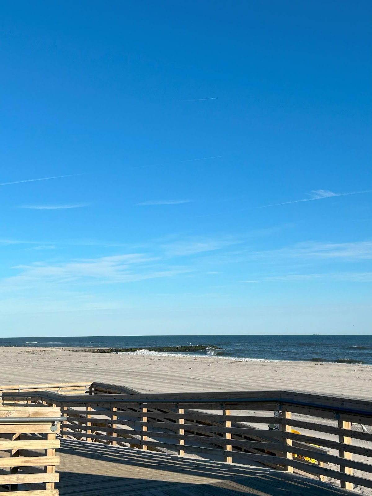 A beach with a railing and a body of water

Description automatically generated