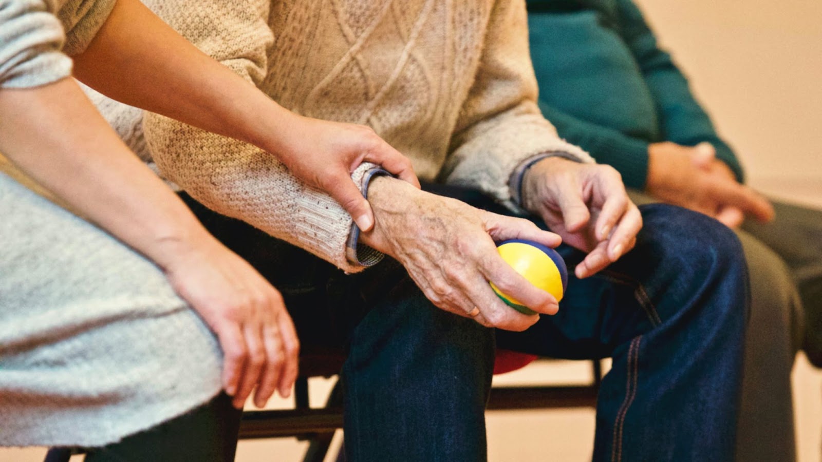 A person holding a senior's hand while the senior holds a ball