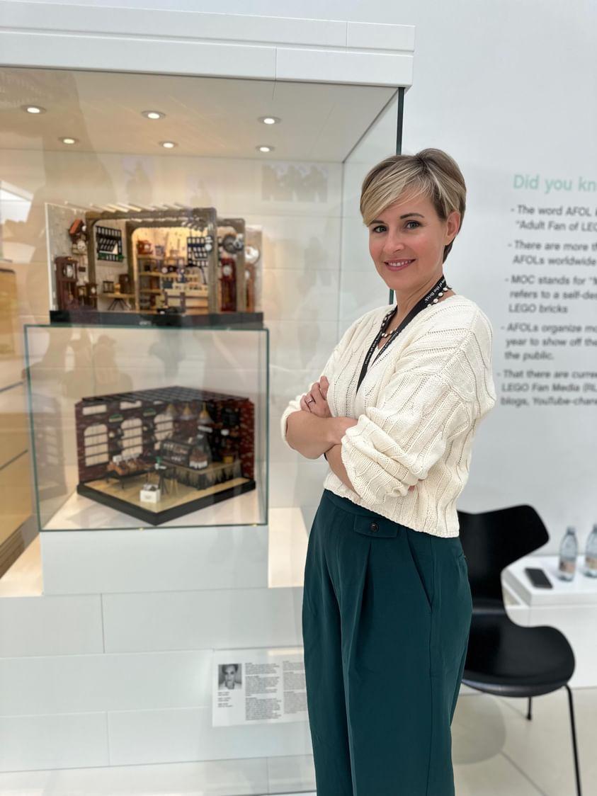 A photo of Kelly Bartlett standing in front of her two creations displayed in the Masterpiece Gallery