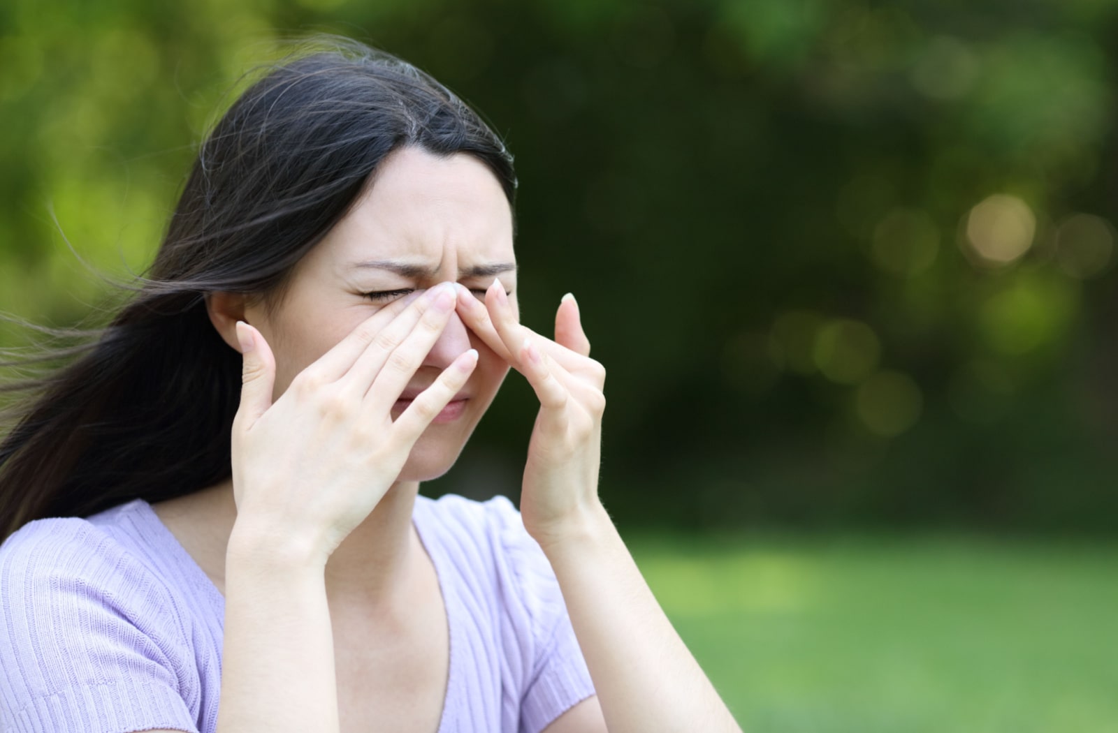 A woman standing outside and she is rubbing her eyes due to irritation
