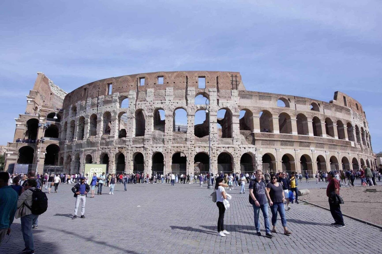 A group of people standing in front of a large stone building with Colosseum in the background