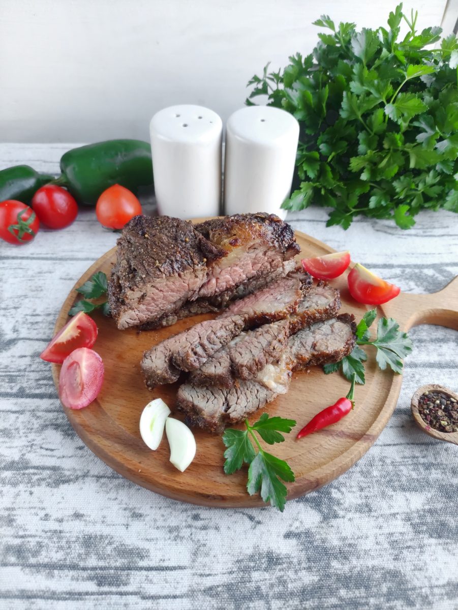 An air-fried ribeye steak is beautifully presented on a wooden cutting board, accompanied by fresh tomatoes and peppers.