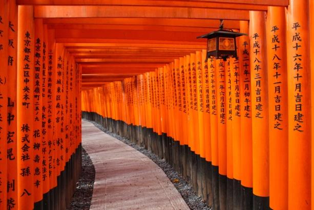 A path with orange pillars with Fushimi Inari-taisha in the background
Description automatically generated