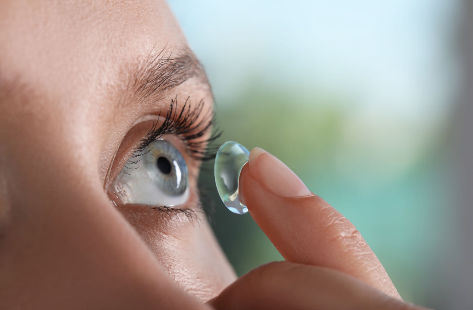 A woman uses her index finger to place a contact lens on her eye