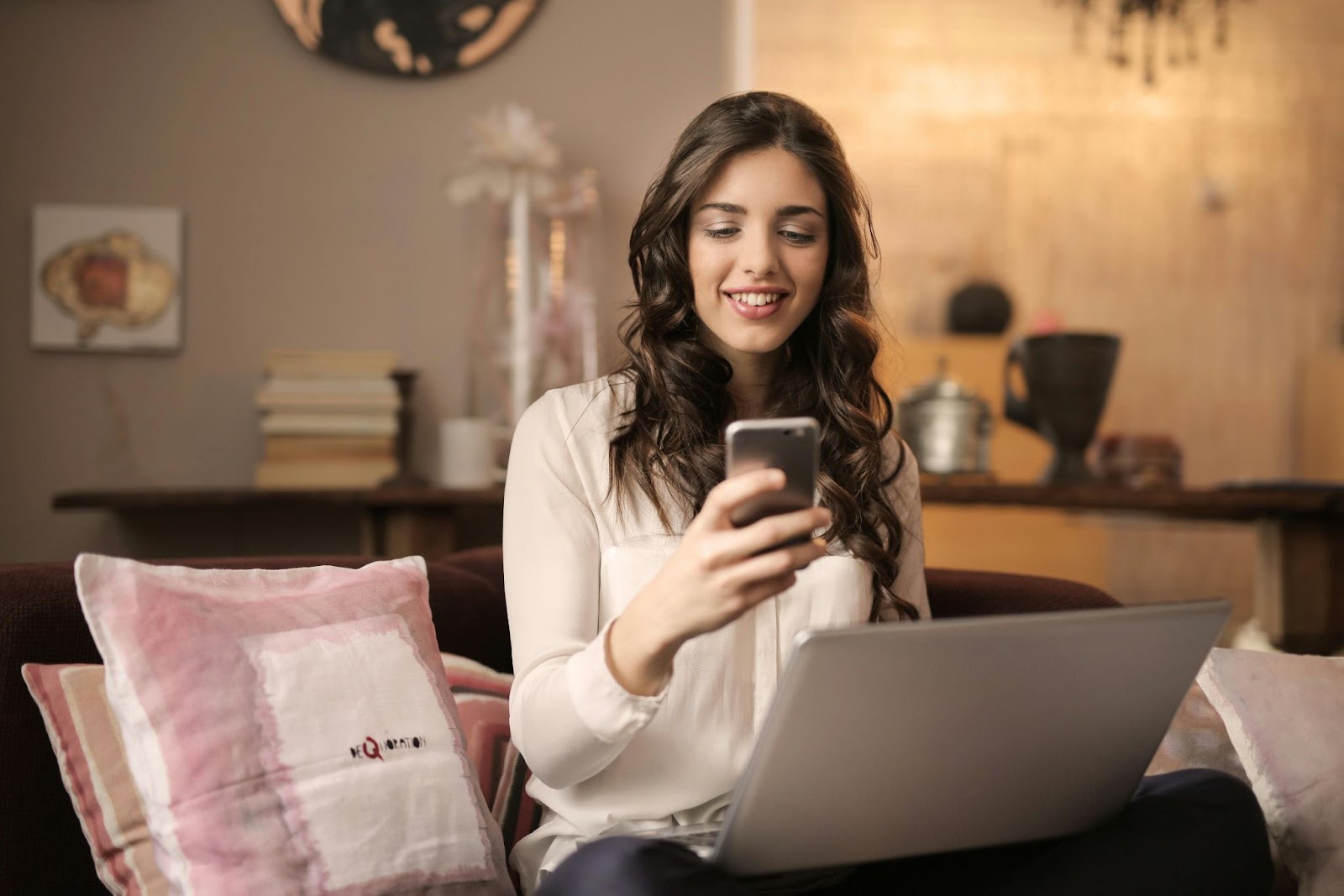 Woman smiling sitting on a couch with a phone and a laptop