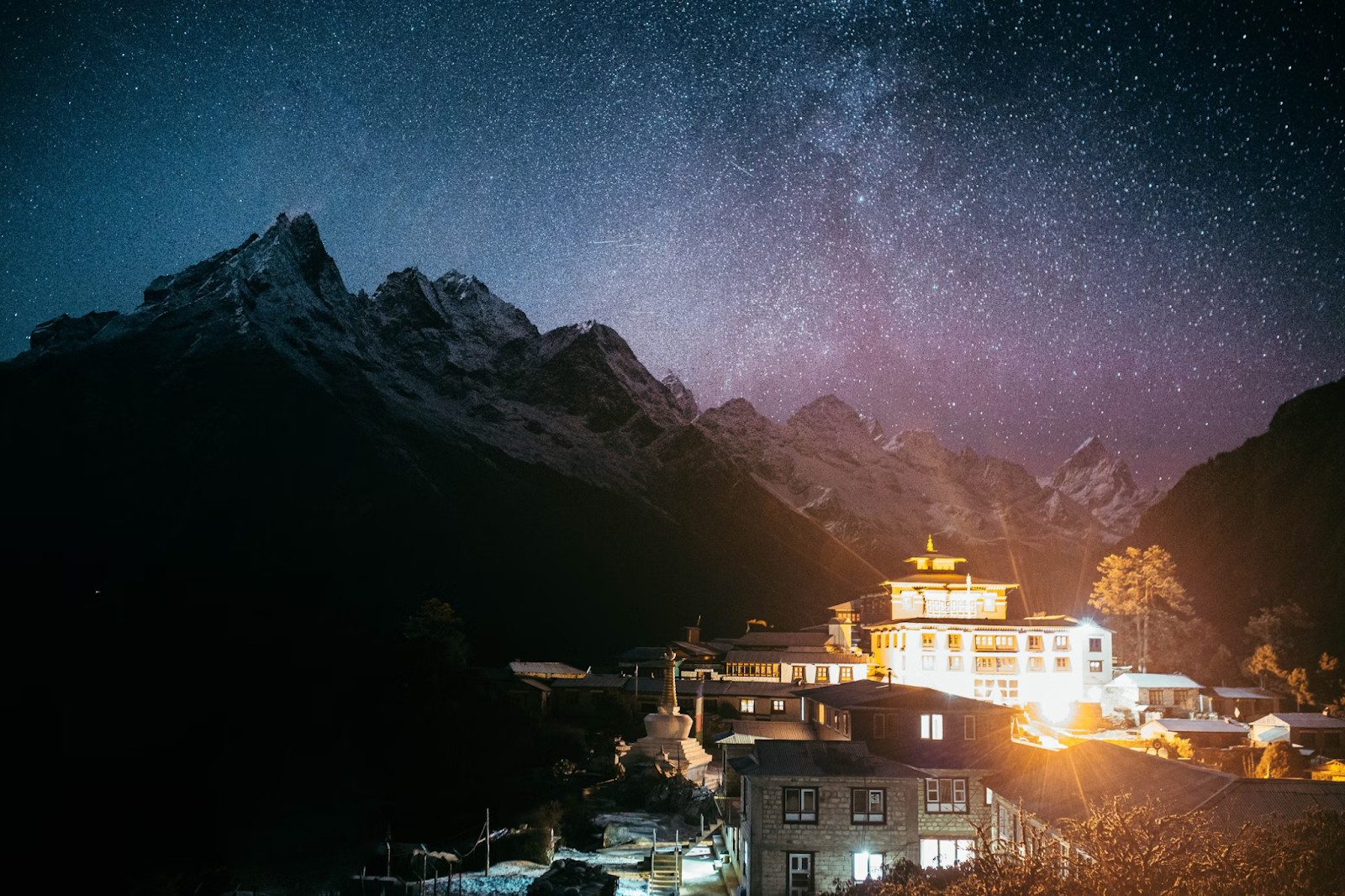 Nighttime view of a lodge in the Everest region, illuminated against a starry sky and surrounded by majestic mountains, highlighting the natural beauty and cultural significance of the area for trekkers.