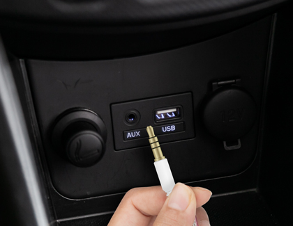 A hand preparing to connect an Aux cable to the Aux port of a car