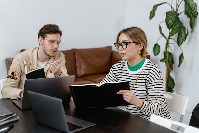 A person discussing to another person with a book and laptop