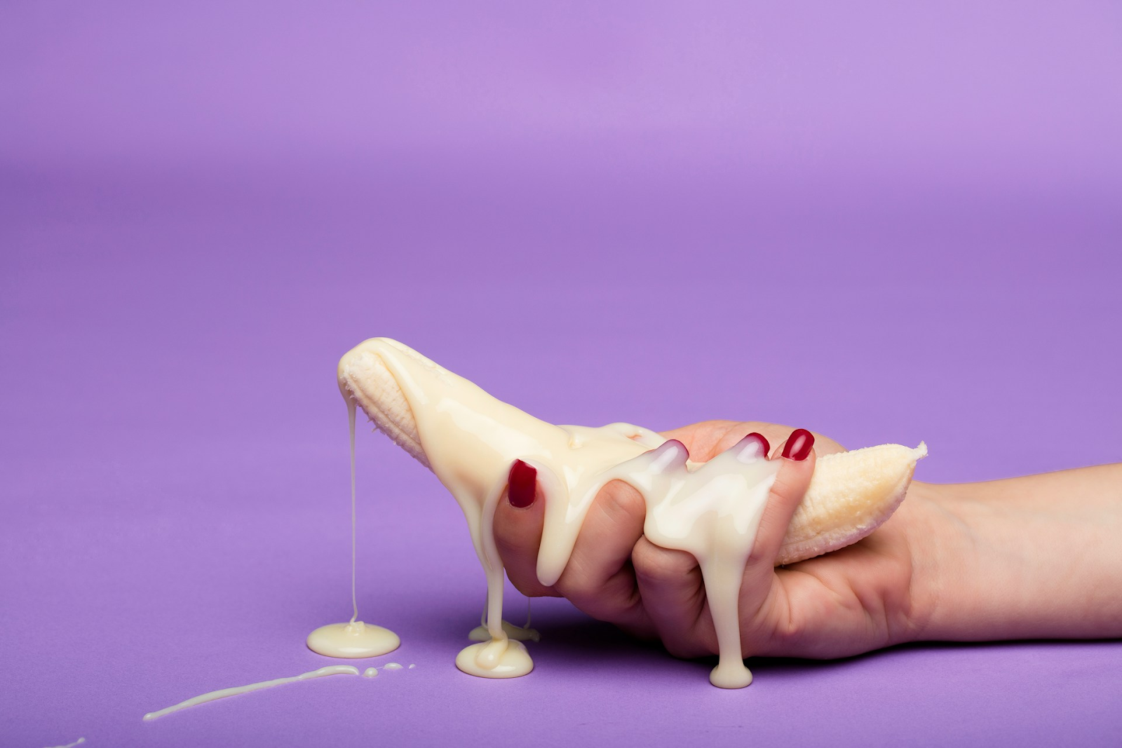A woman holds a banana covered in drippy yoghurt - sexual fruit representing premature ejaculation - A man stands awkwardly in an elevator next to an awkward woman - https://www.pexels.com/photo/a-man-and-a-woman-standing-next-to-each-other-9566326/