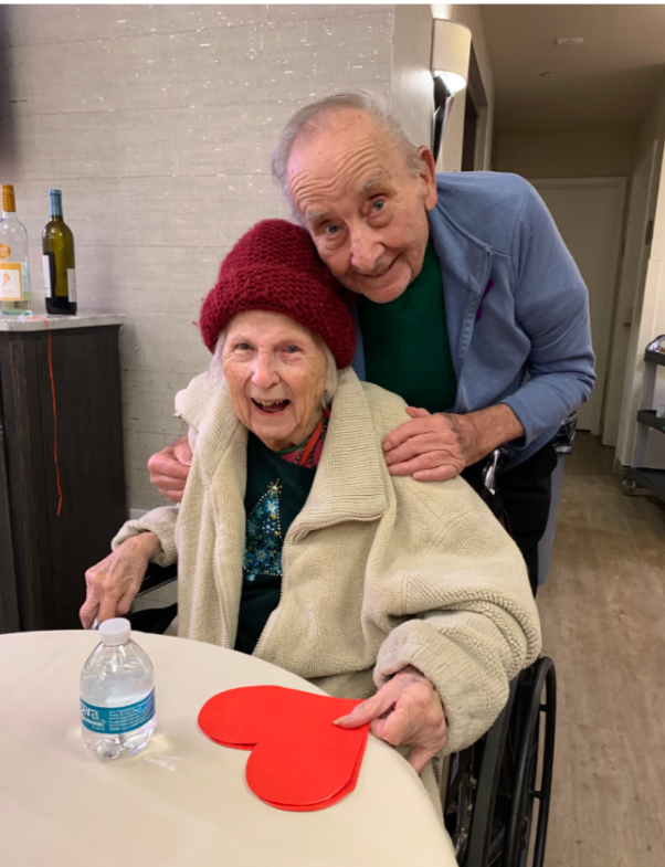 An elderly  couple smiling with a woman holding a cut out piece of paper with a heart