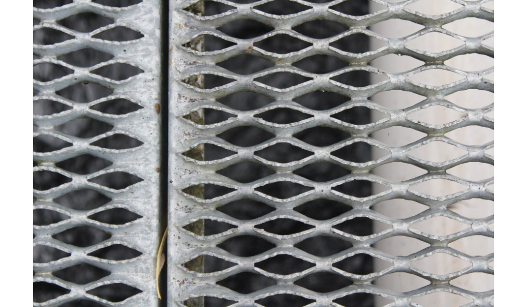 An overhead view of a metallic grate comprised of intersecting rows of oval shaped holes. The holes allow the ability to see through to what's below.