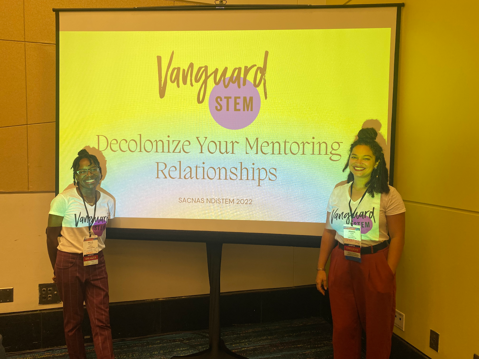 A photo of Dr. Long and Dr. Harriot standing in front of a projector screen showing a presentation titled "Decolonize your mentoring relationships"
