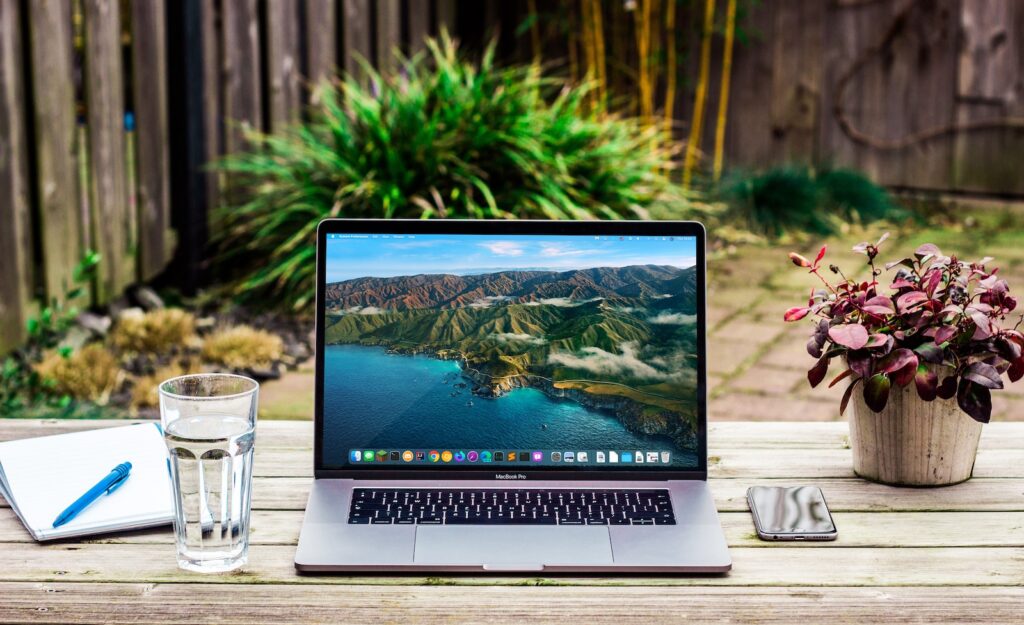 macbook pro beside clear drinking glass on brown wooden table