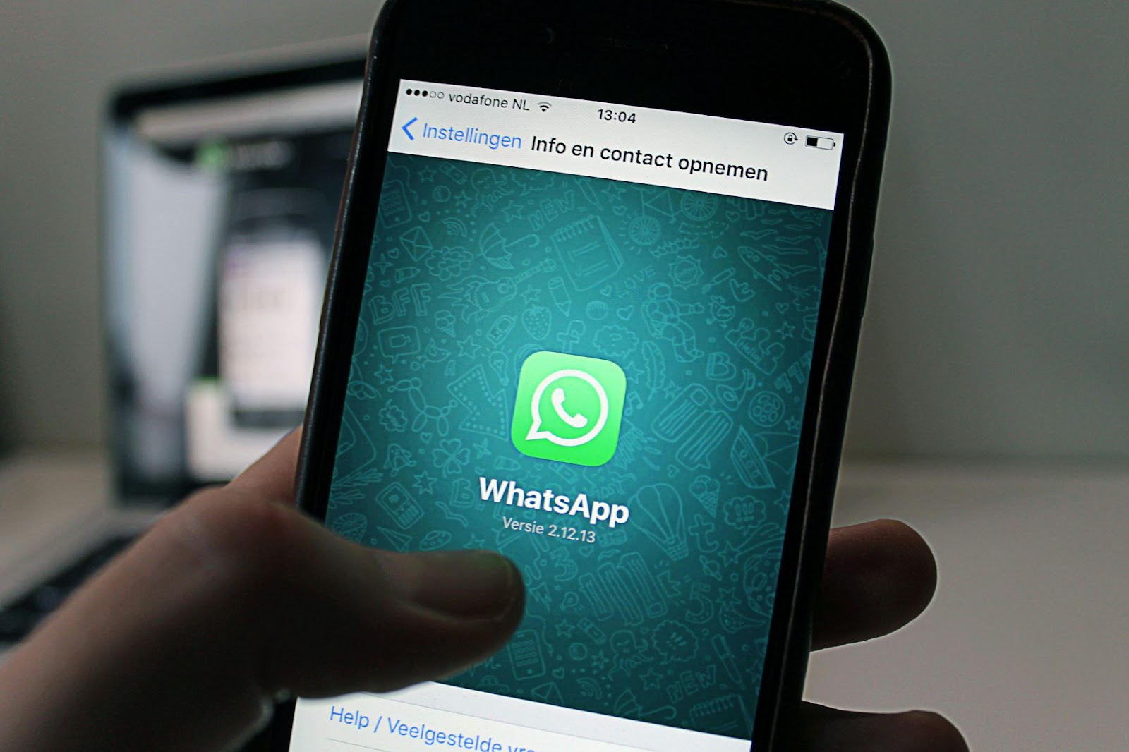 Una mano sosteniendo un teléfono móvil con la pantalla mostrando la aplicación WhatsApp abierta en la sección de información de contacto.