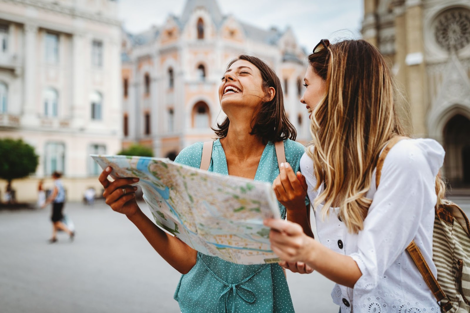 Duas mulheres sorrindo e segurando o mesmo mapa no centro de uma cidade.
