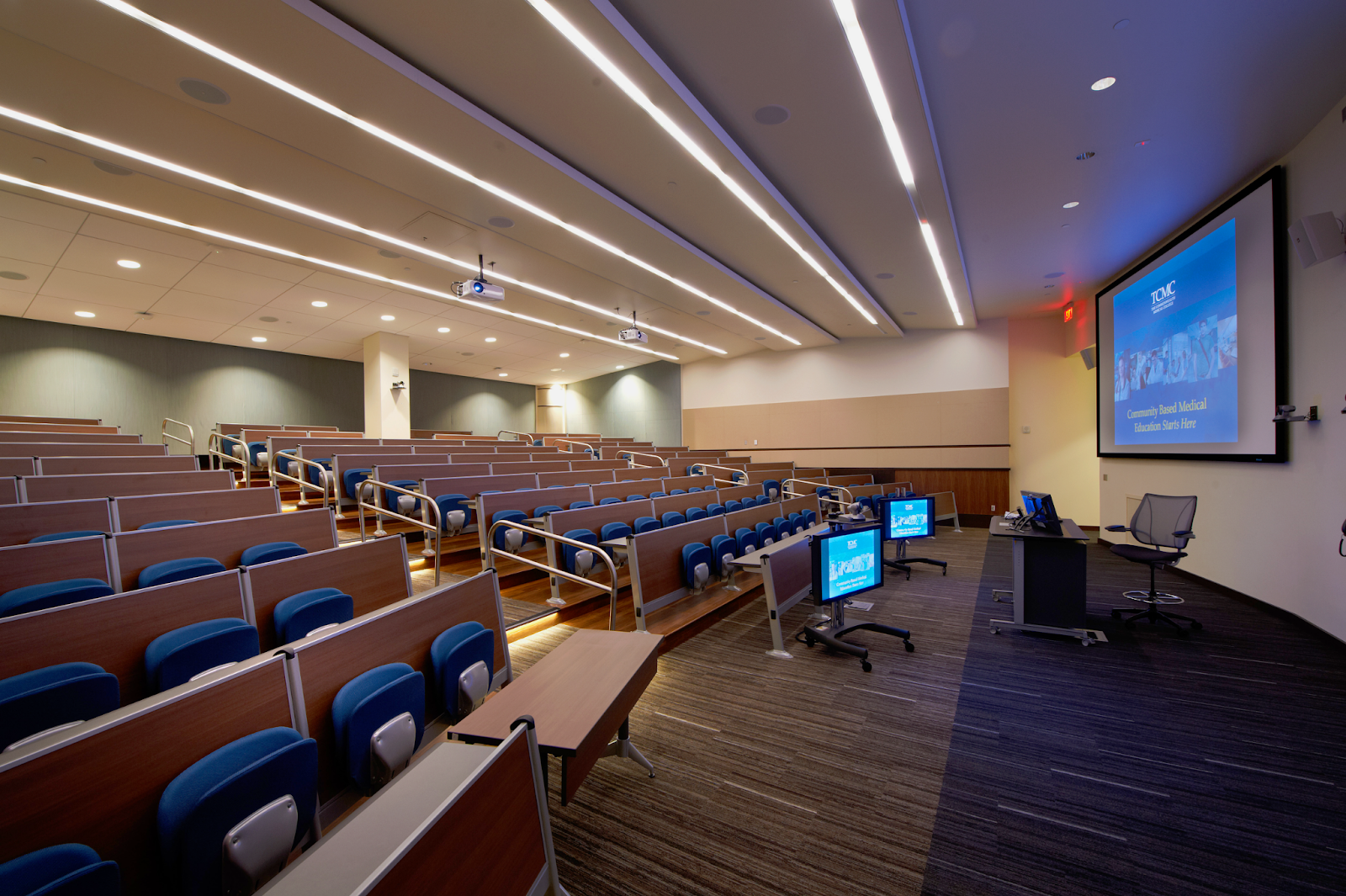 A modern lecture hall with rows of seats and large screens on the walls, where Geisinger Commonwealth School of Medicine students are attending a lecture.