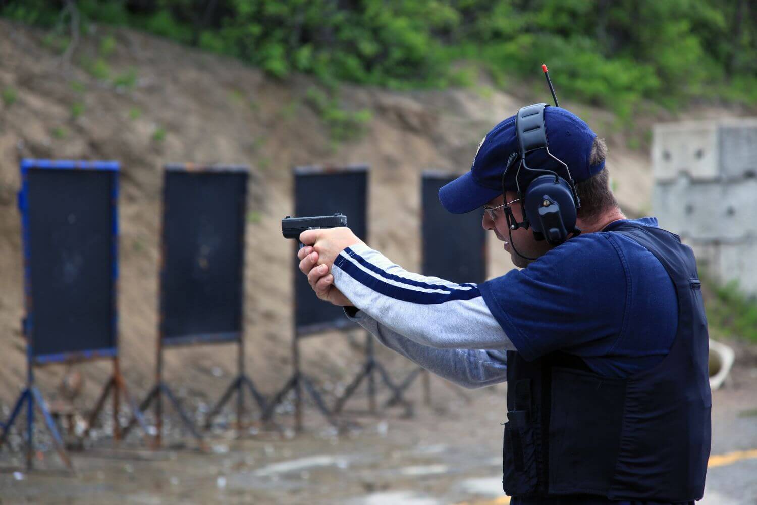 Man wearing protective ear muffs shooting his pistol at an outdoor shooting range