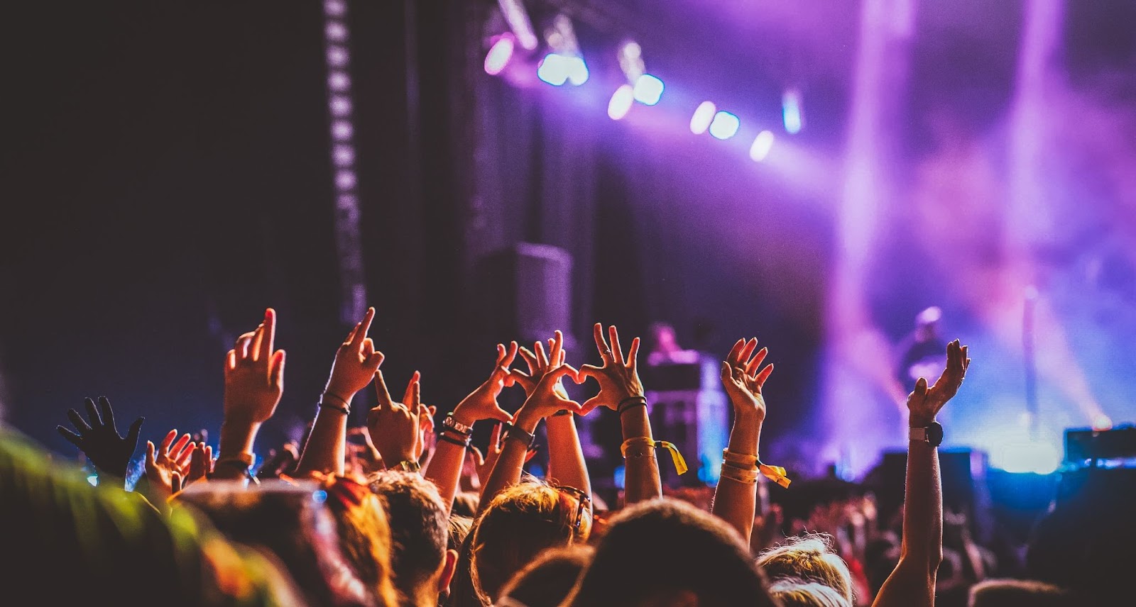 Público em show noturno com diversos braços para cima e, no centro, duas mãos formando um coração.