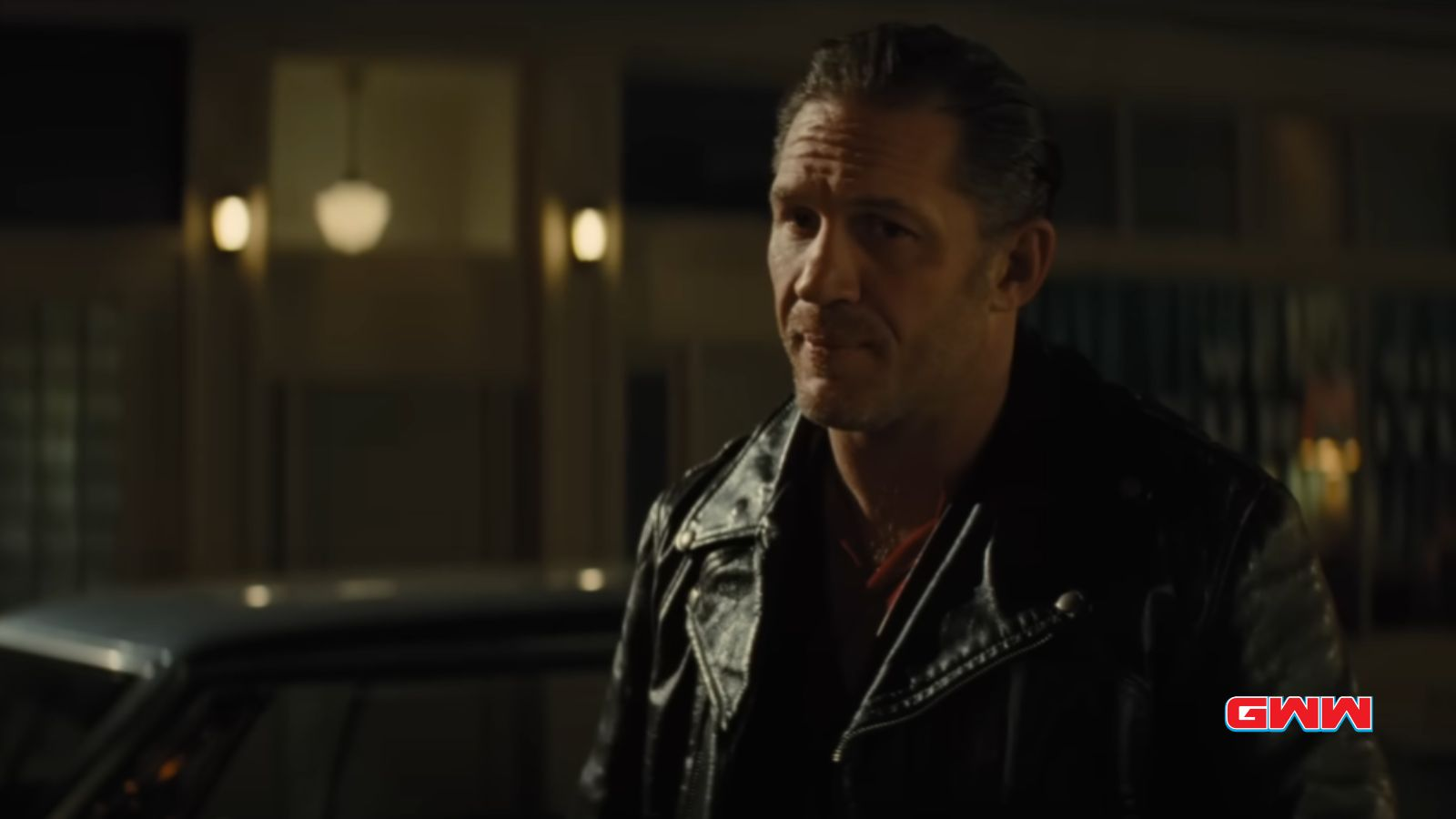 Johnny in a leather jacket speaking at night, standing near a car.
