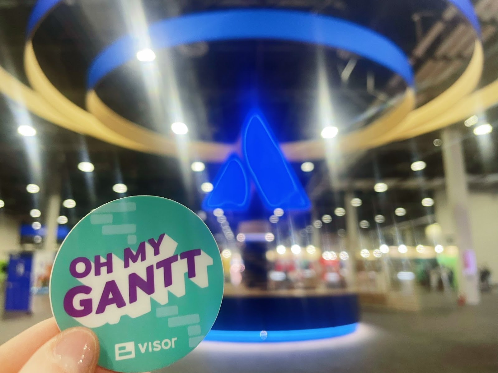 A sticker reading “oh my gantt” held up in front of the Atlassian logo in the expo hall