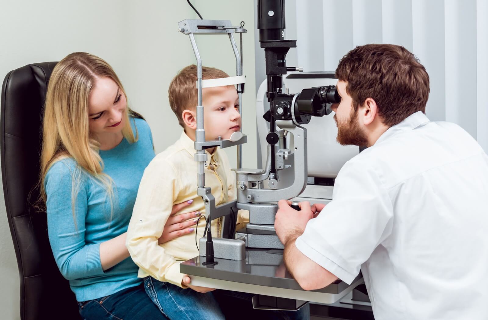 A young boy, who sitting in his mother's lap, getting his eyes checked for myopia.