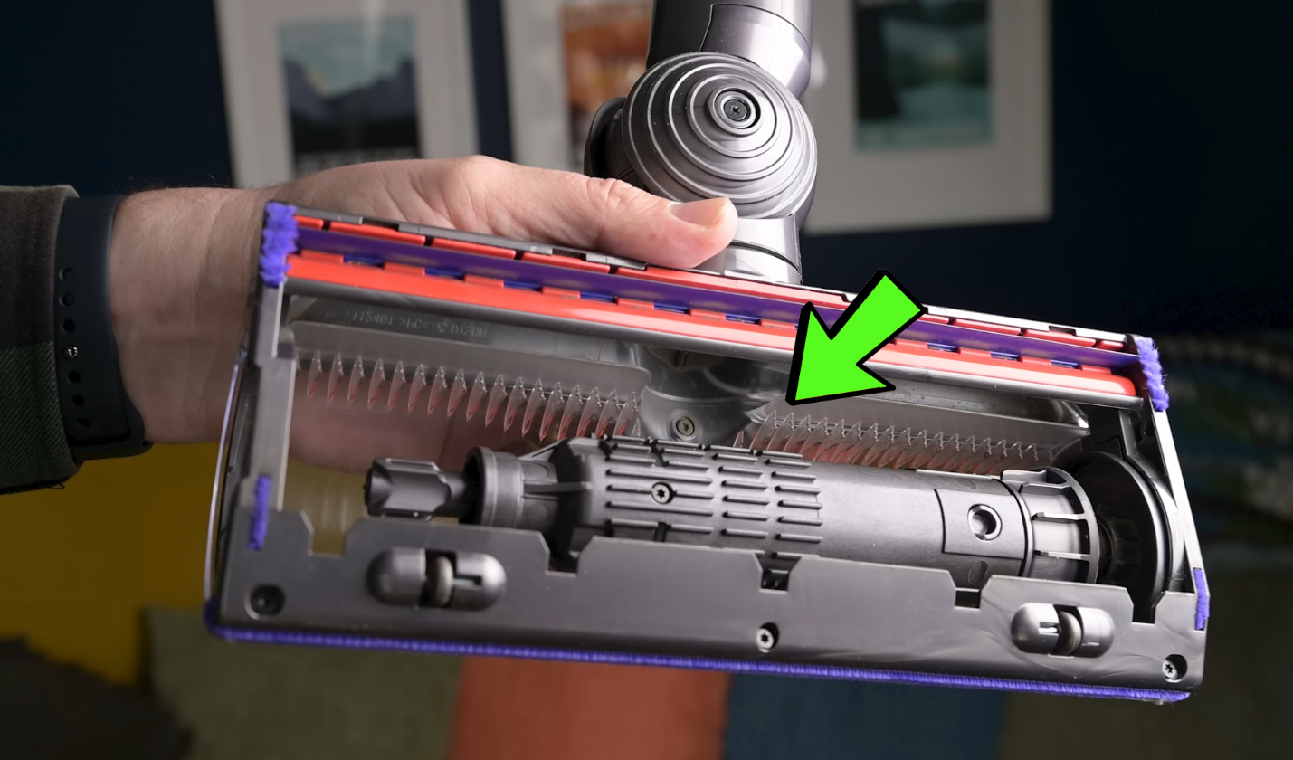 The underside of the Dyson V11's Motorbar cleaner head with an arrow pointing to the red and purple anti-tangle combs, designed for efficient hair removal.