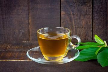 Mitragyna Speciosa Korth or kratom tea in transparent cup wtih green leaf on rustic wooden background.