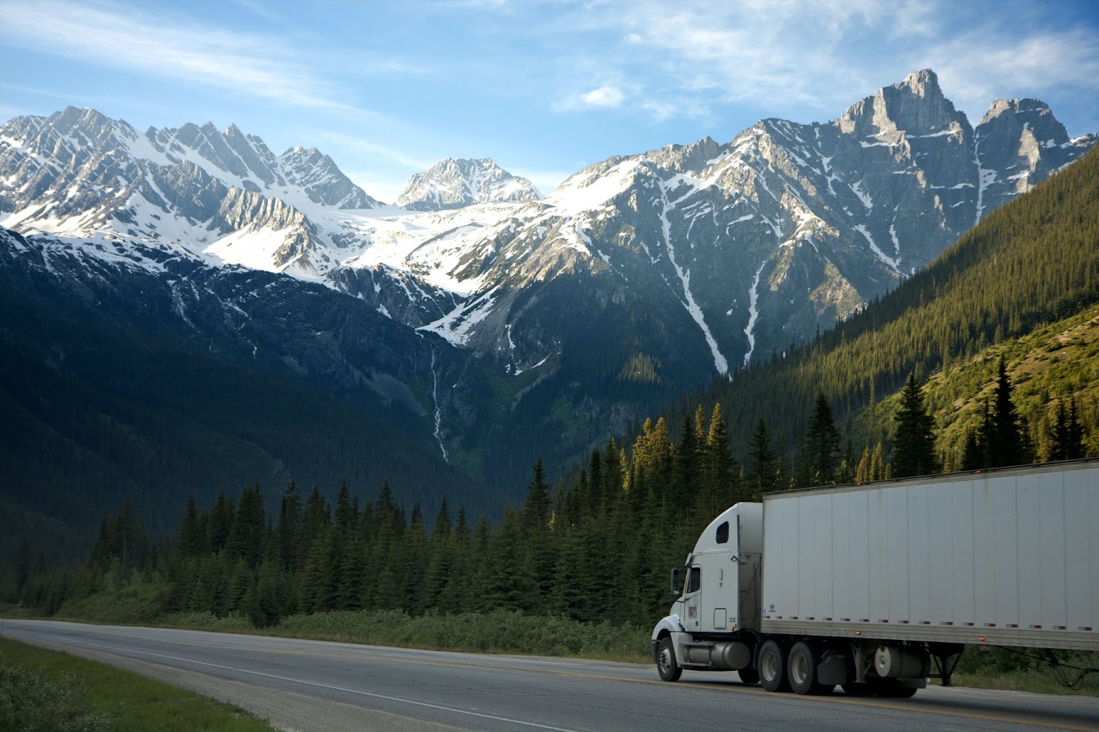 A white semi-truck driving on a mountain road with snow in the background