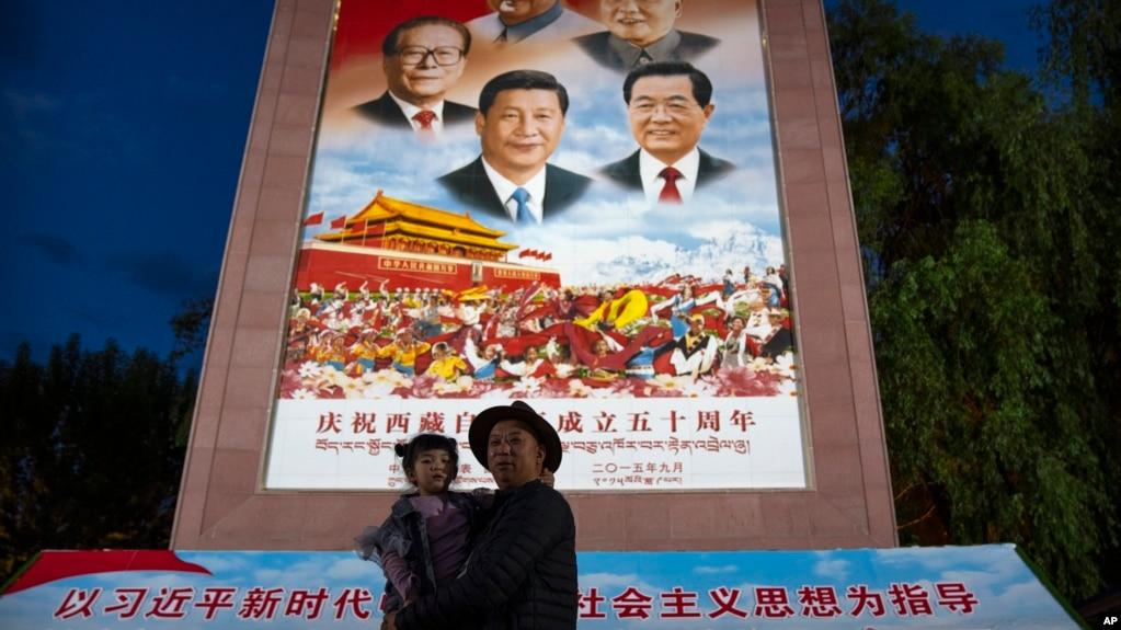 资料照:在西藏拉萨布达拉宫外,一名男子抱着一个小女孩在一幅宣传中国历届领导人的画像前拍照。(2021年6月1日)