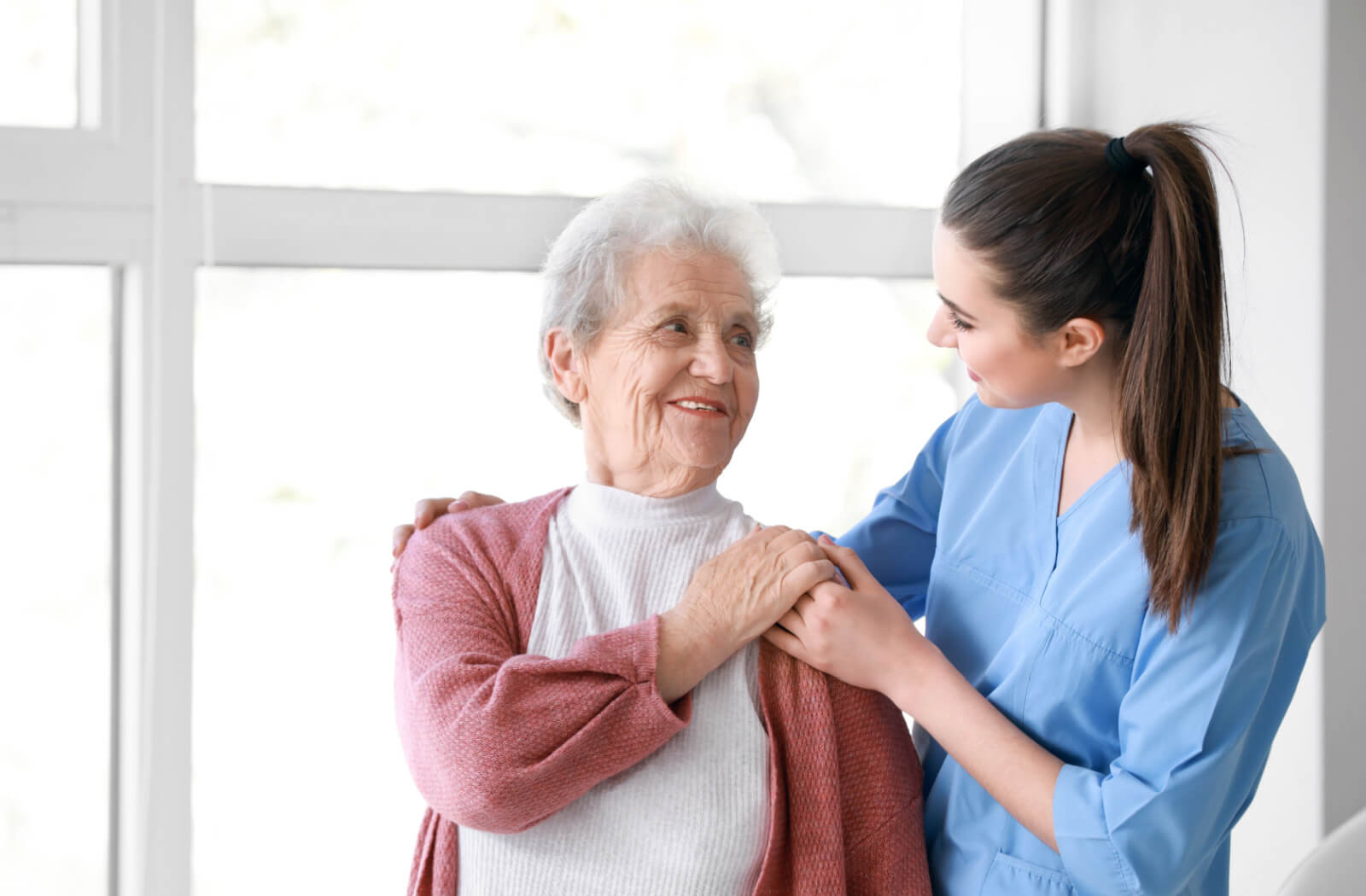 A female medical care professional attends to a senior woman in a senior living community as they both smile