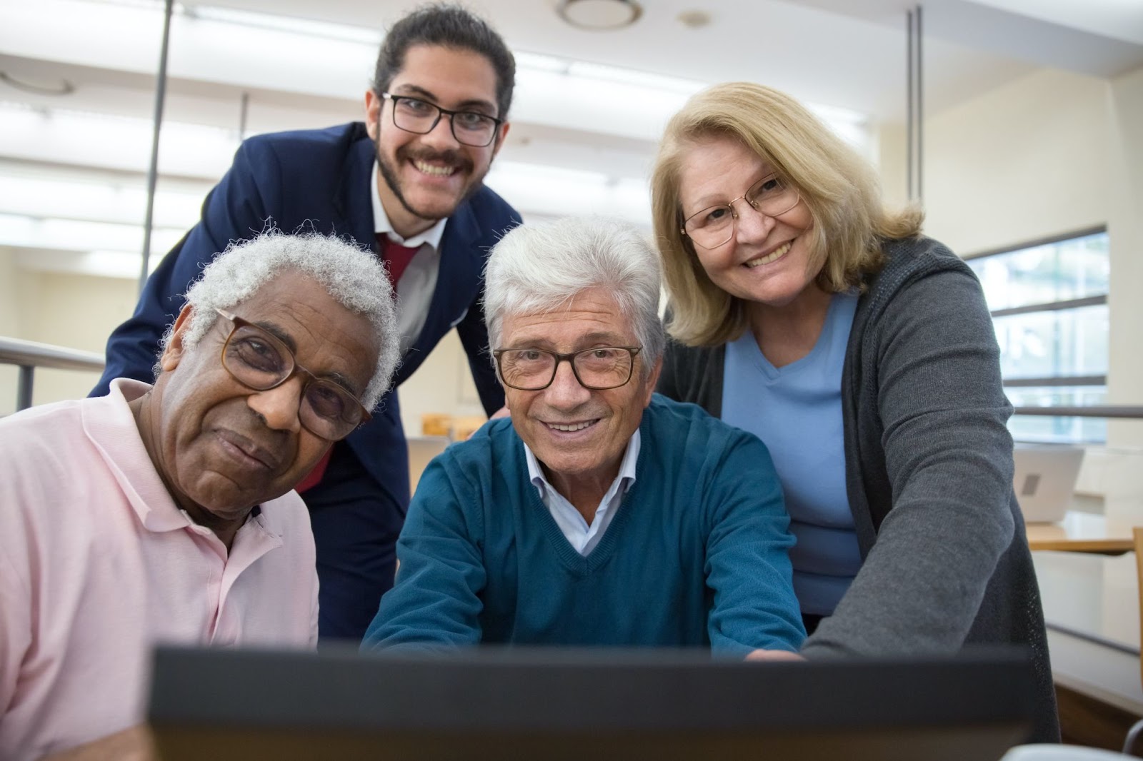A few senior citizens behind a computer screen all smiling at the camera